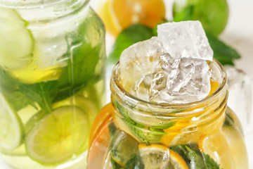 Glass jars with homemade lemonade and ice, citrus slices on a rustic white wooden background. Close-up