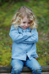 Angry child with long blond hair crossing his arms