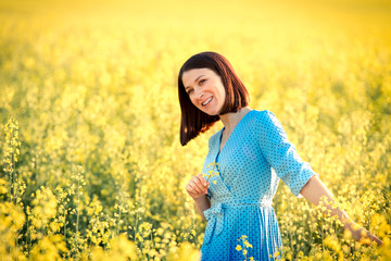 Naklejka na ściany i meble Summer mood. Attractive girl in blue dress in yellow field. Smiling caucasian young woman enjoying summer day.