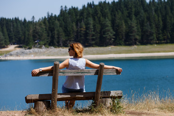 back view of girl on a bench near a mountain lake and pine trees. Black lake, Montenegro