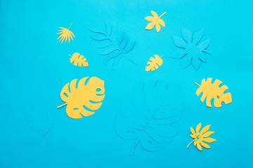 Blue and yellow tropical leaves pattern on a bright blue background. Papercraft flat lay header.