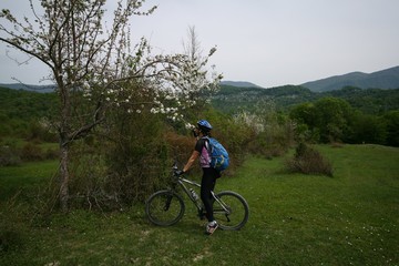 Fototapeta na wymiar Young woman riding a bike near a flowering tree in the mountains