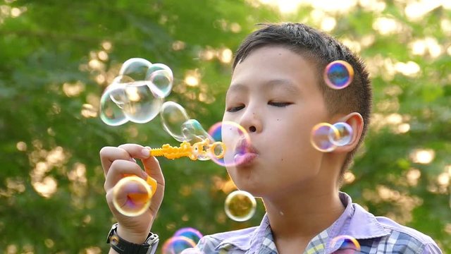 Young asian boy blowing soap bubbles in park ,slow motion.
