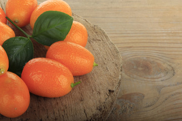 heap of kumquats with green leaves on wooden background