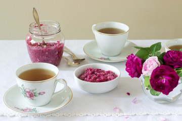 Jam from the petals of the Damascus rose, a cup of green tea and a vase of roses on a light table....