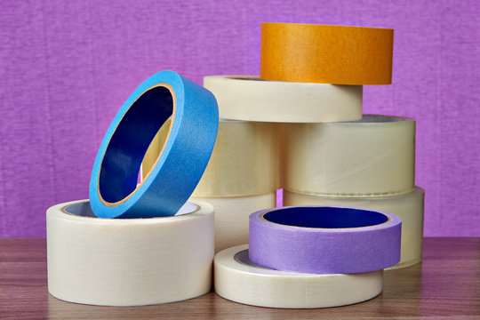 Heap of multicolor and multipurpose adhesive tape rolls, on purple background.