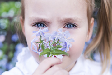 Portrait of a beautiful little blue-eyed girl sniffing a flower, close-up