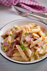 Penne pasta with bacon and sundried tomatoes. Alfredo penne pasta on white plate on wooden table. vertical