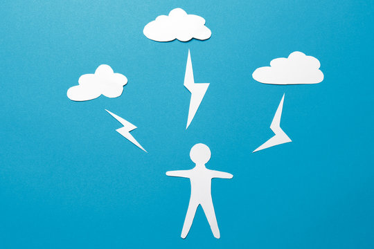 The concept of man is under threat. A paper man origami stands under lightning from the clouds on a blue background. Lightning strikes an unprotected person. Danger to life