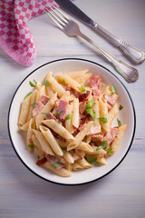 Penne pasta with bacon and sundried tomatoes. Alfredo penne pasta on white plate on wooden table. overhead, vertical