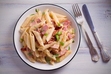 Penne pasta with bacon and sundried tomatoes. Alfredo penne pasta on white plate on wooden table. overhead, horizontal