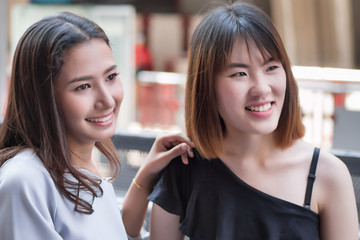 two women looking up, looking away watching something; portrait of young woman with her friend looking away in urban environment; asian 20s young adult woman model