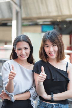 successful girl pointing thumb up for success; two women giving thumb up to you; portrait of cheerful smiling women pointing up approving, yes, ok, good, thumb up gesture; asian woman 20s adult model