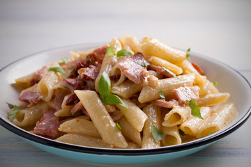 Penne pasta with bacon and sundried tomatoes. Alfredo penne pasta on white plate on wooden table. horizontal