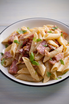 Penne pasta with bacon and sundried tomatoes. Alfredo penne pasta on white plate on wooden table. vertical