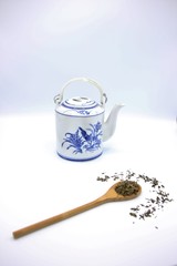 Wooden spoon with green tea leaves and chinese teapot isolated on white