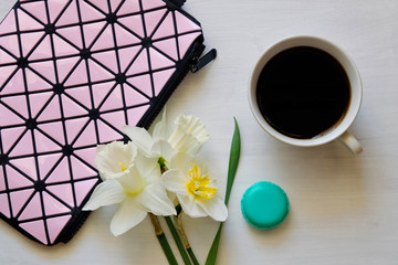 Cosmetic bag, cup of coffee, macaroons and daffodils on white background