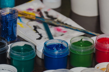 different colour paint in bottles closeup with used brushes and white painted napkins