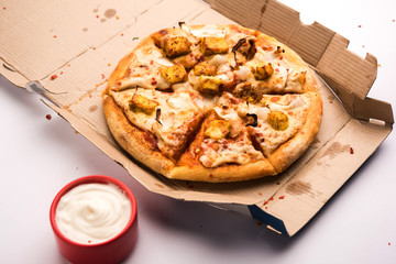 Paneer Pizza is an indian version of Italian dish topped with Cottage Cheese, served in a plate with white sauce. selective focus