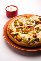 Paneer Pizza is an indian version of Italian dish topped with Cottage Cheese, served in a plate with white sauce. selective focus