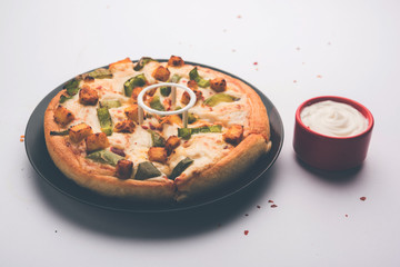 Paneer Pizza is an indian version of Italian dish topped with Cottage Cheese, served in a plate with white sauce. selective focus