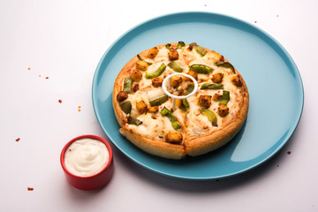 Paneer Pizza is an indian version of Italian dish topped with Cottage Cheese, served in a plate with white sauce. selective focus