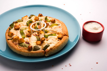 Paneer Pizza is an indian version of Italian dish topped with Cottage Cheese, served in a plate with white sauce. selective focus