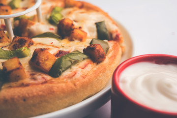 Paneer Pizza is an indian version of Italian dish topped with Cottage Cheese, served in a plate with white sauce. selective focus
