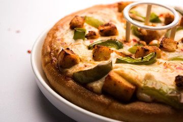 Paneer Pizza is an indian version of Italian dish topped with Cottage Cheese, served in a plate with white sauce. selective focus