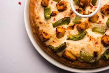 Paneer Pizza is an indian version of Italian dish topped with Cottage Cheese, served in a plate with white sauce. selective focus