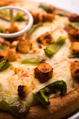 Paneer Pizza is an indian version of Italian dish topped with Cottage Cheese, served in a plate with white sauce. selective focus