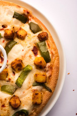 Paneer Pizza is an indian version of Italian dish topped with Cottage Cheese, served in a plate with white sauce. selective focus