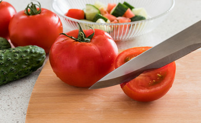 Making salad in the kitchen. Tomato and cucumber, wooden board and knife