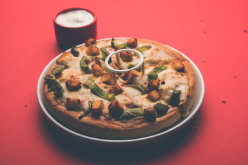 Paneer Pizza is an indian version of Italian dish topped with Cottage Cheese, served in a plate with white sauce. selective focus