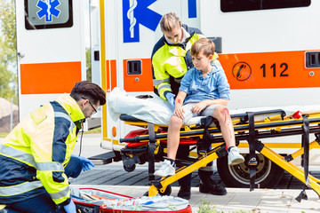 Emergency doctors caring for accident victim boy sitting on stretcher