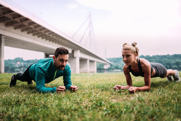 Naklejka premium Plank exercise at the park. Two fit people workout outdoors.