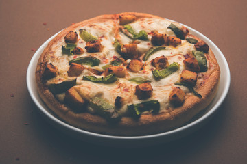 Paneer Pizza is an indian version of Italian dish topped with Cottage Cheese, served in a plate with white sauce. selective focus