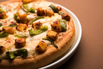 Paneer Pizza is an indian version of Italian dish topped with Cottage Cheese, served in a plate with white sauce. selective focus