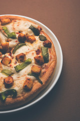 Paneer Pizza is an indian version of Italian dish topped with Cottage Cheese, served in a plate with white sauce. selective focus