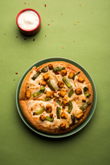 Paneer Pizza is an indian version of Italian dish topped with Cottage Cheese, served in a plate with white sauce. selective focus