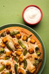 Paneer Pizza is an indian version of Italian dish topped with Cottage Cheese, served in a plate with white sauce. selective focus