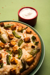 Paneer Pizza is an indian version of Italian dish topped with Cottage Cheese, served in a plate with white sauce. selective focus