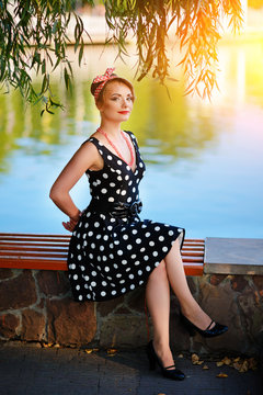 A beautiful young woman dressed sits on a bench near the pond