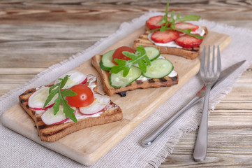 Sandwiches with cream cheese, radish, fresh cucumber, strawberries and arugula.