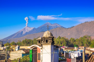 Beautiful landscape of huge mountain in process of aruption with a column of ash, view from the rooftops of the building in Antigua city in gorgeous sunny day and blue sky