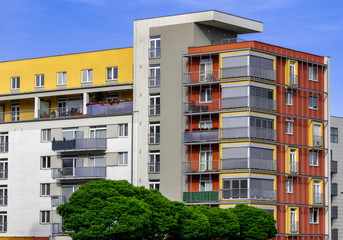 Modern apartments with white, yellow and red colours behind trees