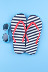 Flip-flops with a blue sunglasses on a blue background. Top view. Beach accessories
