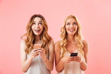 Two cheerful pretty women in pajamas holding smartphones