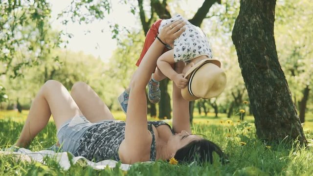 Happy smiling mother with little son in hat on picnic under big tree at park. Concept of happy family love