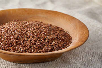Flax seeds in a wooden plate on homespun tablecloth, top view, close-up.